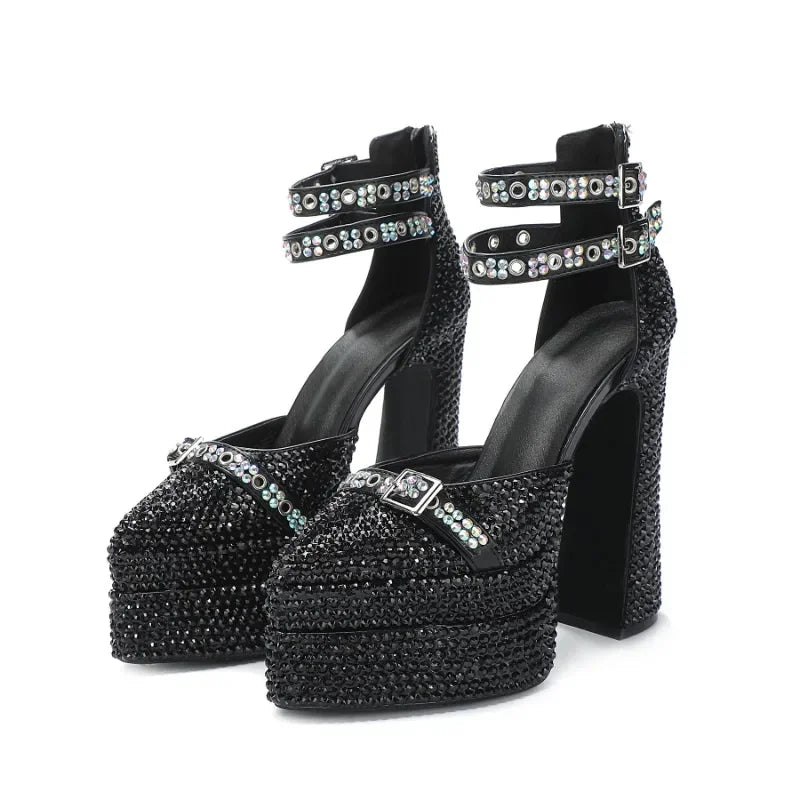 Front angle showing black open-toe platform sandals with a sparkling pearl bow detail and a buckle strap wrapping the ankle.