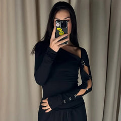 Mirror selfie in a black asymmetric off-shoulder top with sleek cutouts, styled for a clean, modern silhouette against soft curtains.