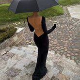 Back view of a black long sleeve mermaid maxi dress with an open back and fine chain detail, styled with an umbrella outdoors.