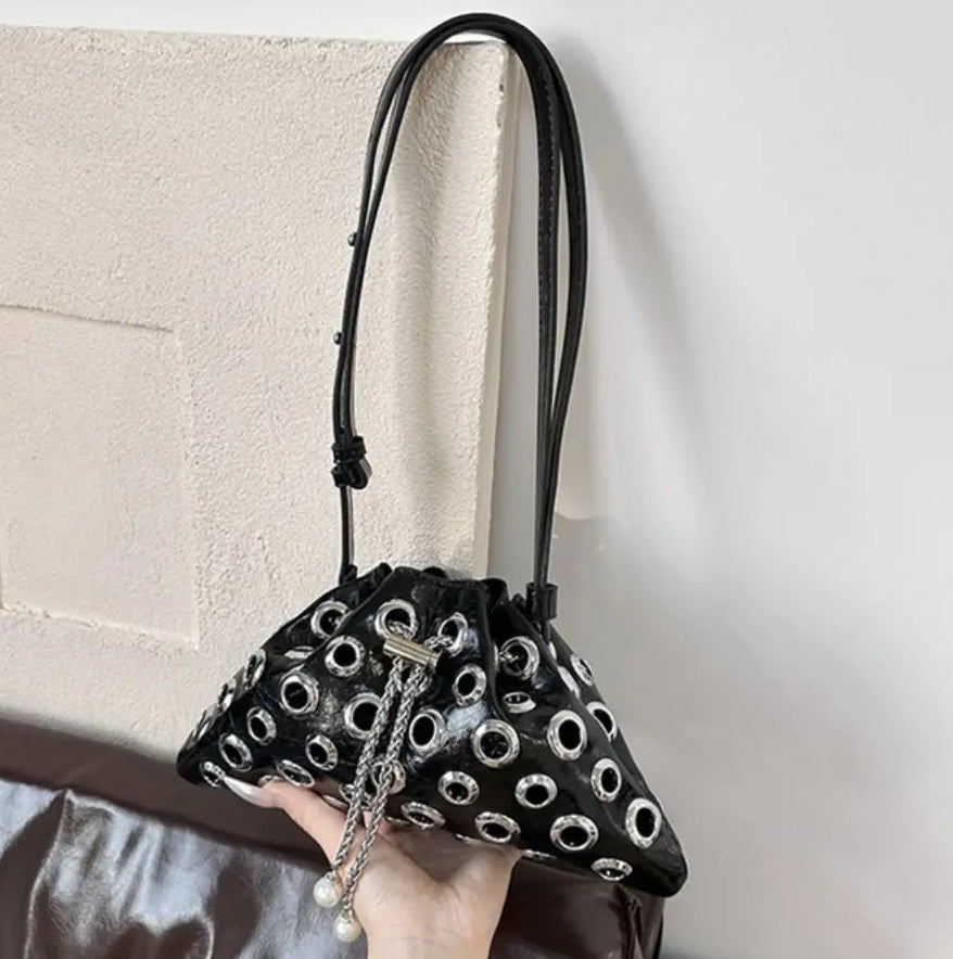Hand-held view of the compact black bag, showing its structured shape and statement hardware designed to sit neatly under the arm.