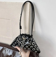 Hand-held view of the compact black bag, showing its structured shape and statement hardware designed to sit neatly under the arm.
