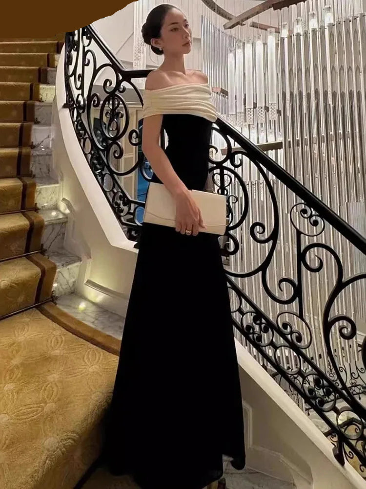A woman in a Black contrast evening dress with an ankle-length, sleek silhouette standing on a staircase with decorative railings.