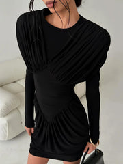 Black long sleeve mini dress with wrapped-look pleating shown in a neutral room