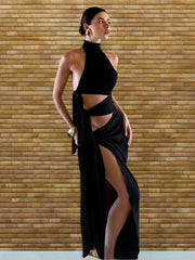 A woman wearing a black hollow-out high split maxi party dress styled for a club night in a room with a brick wall.