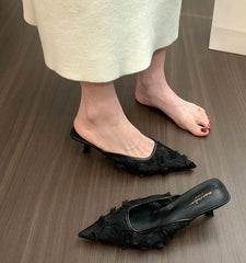 Black lace pointed toe mule heels styled on wooden floor