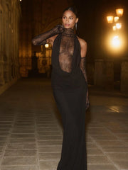 Woman in a black lace turtleneck long dress with gloves styled for formal evenings walking in an elegant setting.