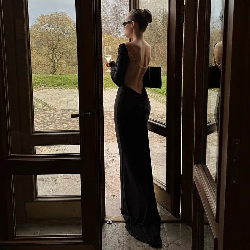 Front angle of a black floor-length gown with slash neckline and slim long sleeves, creating a clean, sculpted formal silhouette.