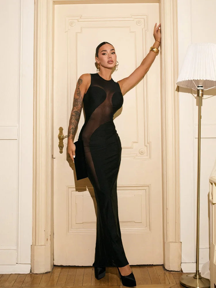 Woman wearing black mesh patchwork sheath maxi dress in elegant setting standing in a room with a white door and lamp.