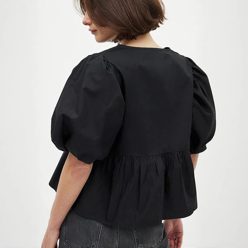Three-quarter angle of a black puff sleeve blouse highlighting sleeve volume and structured shape, paired with denim for a refined casual outfit.