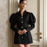 Woman wearing a black mini dress with puff sleeves and gold buttons.