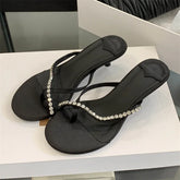 Black sandals with crystal embellishments on a white surface
