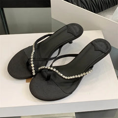Black sandals with crystal embellishments on a white surface