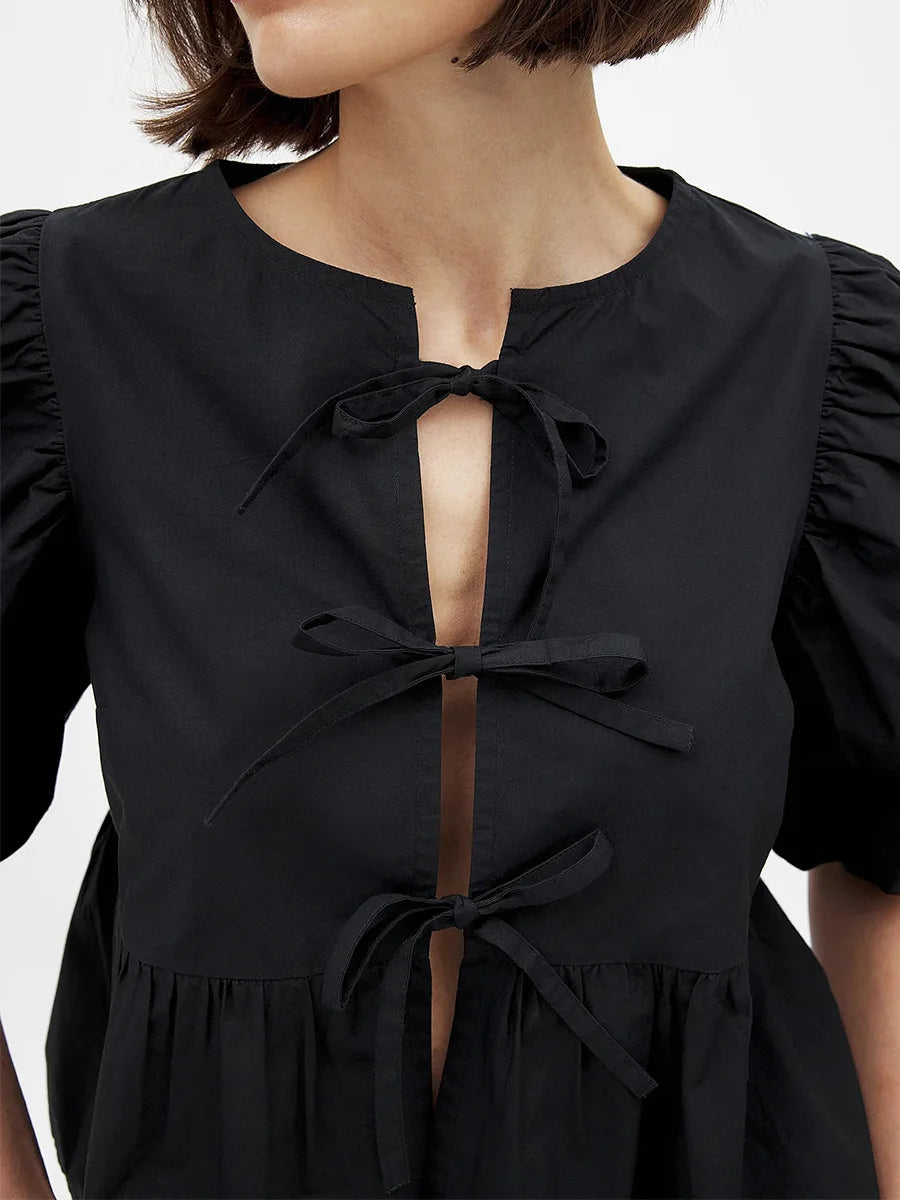 Close-up of the black tie-front neckline with bow detailing, showing the keyhole opening and smooth fabric texture in bright light.