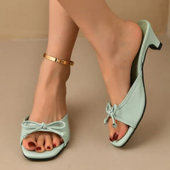 Light blue high-heeled sandals with bow details worn by a person on a beige background