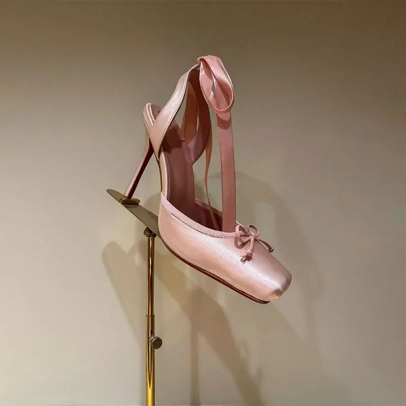 Pink high-heeled shoe on a gold stand against a beige background