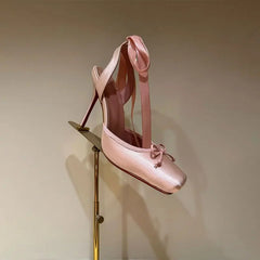 Pink high-heeled shoe on a gold stand against a beige background
