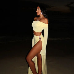 Woman in a bohemian two-piece beach outfit with crop top and skirt standing against a dark background of a beach.
