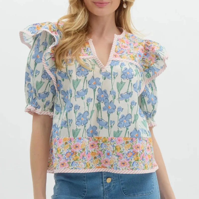 Close view of ruffle trim and floral print on a lightweight blouse with short puff sleeves and a flattering neckline.