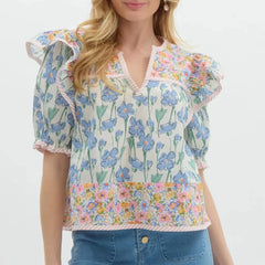 Close view of ruffle trim and floral print on a lightweight blouse with short puff sleeves and a flattering neckline.