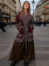 Woman in a deep burgundy printed knit cardigan, belted at the waist, smiling on a city street with classic buildings behind.