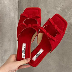Bow flats red women’s slippers for cozy summer outdoor style held by a hand against a gray background