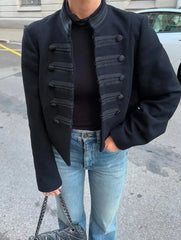 Close-up of tonal braided panels and button-front detailing on a black cropped jacket, showing the structured tailoring and clean finish.