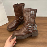 Brown metal buckle mid-calf motorcycle boots with a stable block heel on a wooden surface, held by a hand.