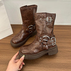 Brown metal buckle mid-calf motorcycle boots with a stable block heel on a wooden surface, held by a hand.