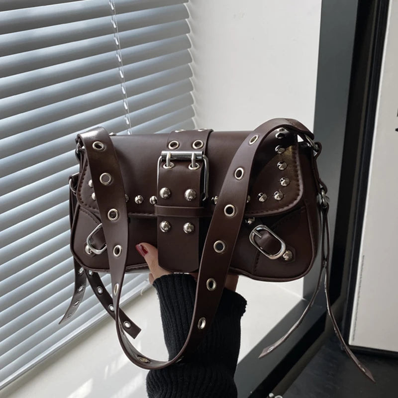 Brown baguette shoulder bag with rivet-style hardware held near a window with blinds, showing the compact shape and strap detailing.