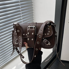 Brown baguette shoulder bag with rivet-style hardware held near a window with blinds, showing the compact shape and strap detailing.