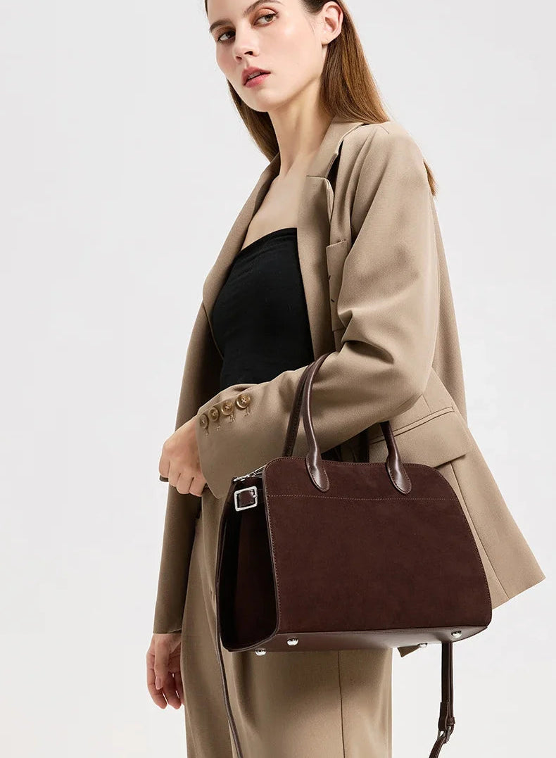 Styled shot of a brown suede leather bag paired with a tailored blazer, giving a polished work-to-weekend look.