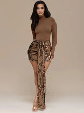 Woman wearing a brown long-sleeve top and gold sequin draped mini skirt on a beige background