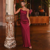 Woman posing in a burgundy satin maxi dress beside a vintage column, showing the square neckline and floor-length A-line sweep.