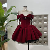 Mannequin in a burgundy velvet off-shoulder corset mini dress with a bow and pleated puff skirt in a studio setting.