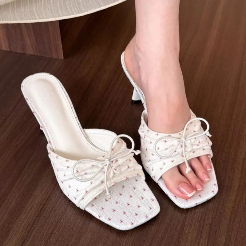 White open-toe shoes with bow details on a wooden floor