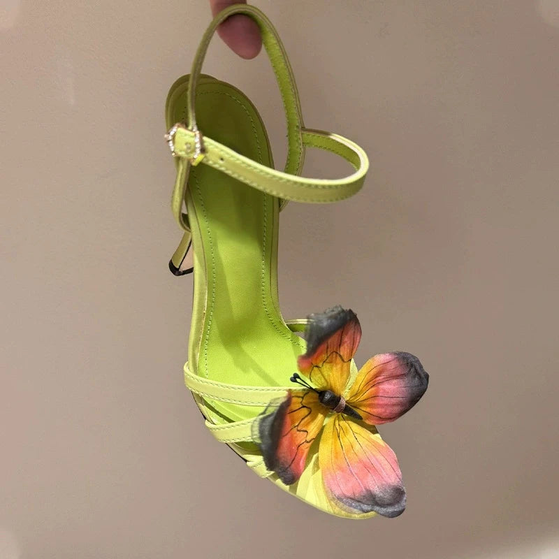 Green sandal with a butterfly motif, high heel party shoes for women, shown on a beige background.