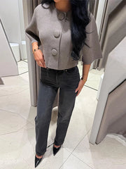 Mirror styling photo of a woman in a gray cropped knit cardigan with oversized buttons, paired with dark jeans and pointed heels.