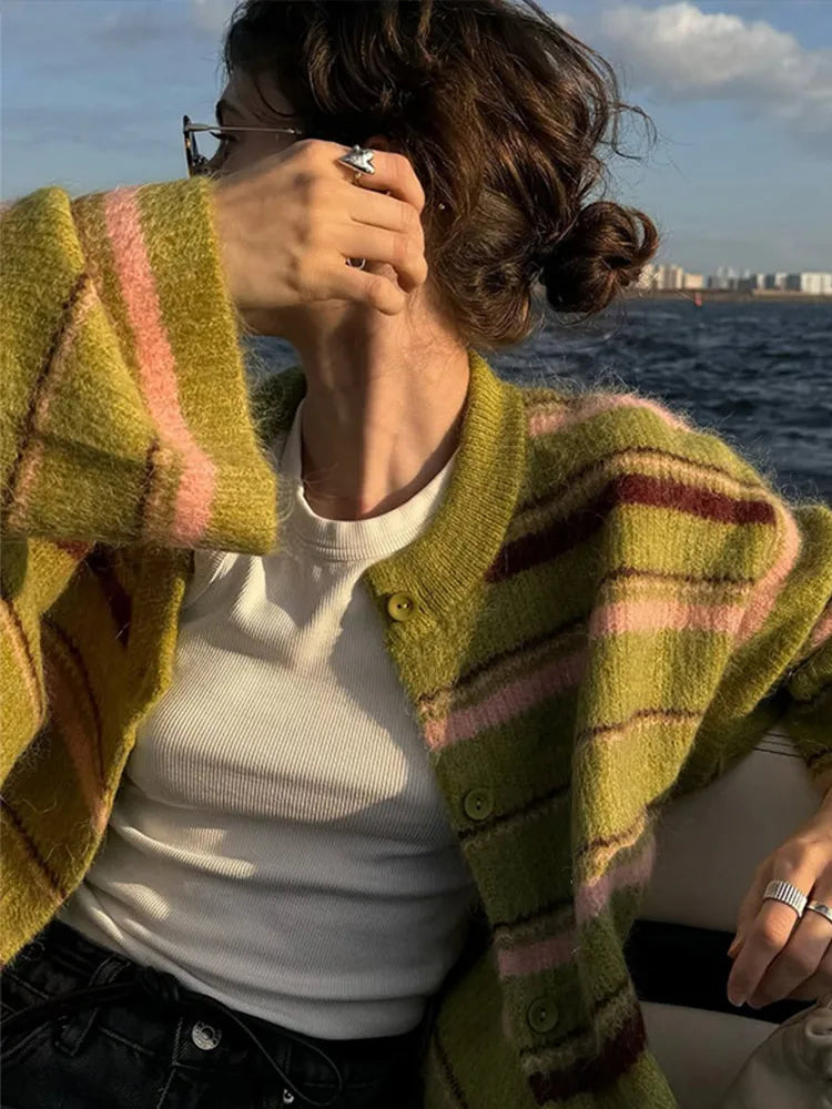 Person wearing a green cardigan with pink stripes by the water