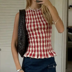 Person wearing a red and white checkered top detail of gathered waist and flutter hem on vintage-style with blue pants, holding a black bag.