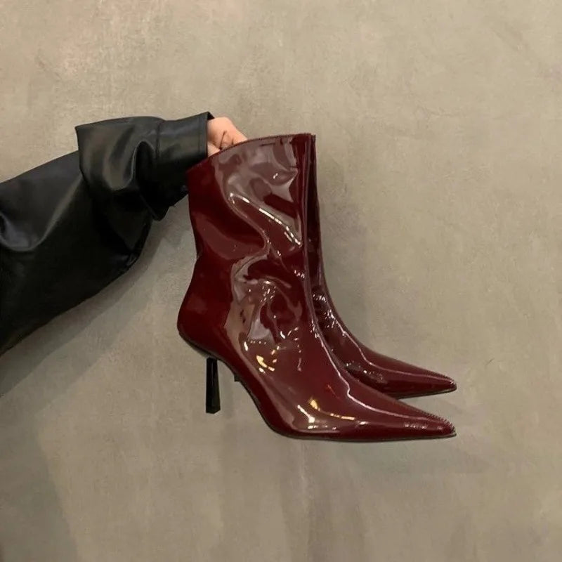 Shiny, cherry red patent ankle stiletto boots displayed for autumn workwear, being held against a neutral background