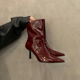 Shiny, cherry red patent ankle stiletto boots displayed for autumn workwear, being held against a neutral background