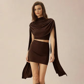 Model wearing a chocolate-brown draped shawl top with scarf detail and matching fitted mini skirt on a neutral background.