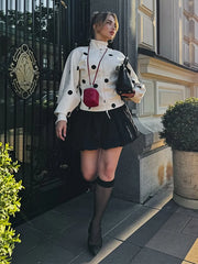 A woman in a polka dot blouse and black skirt standing in front of a building entrance.