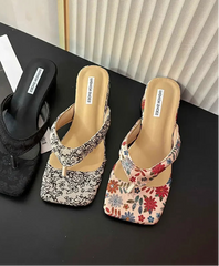 Three pairs of comfort party outdoor floral slippers for relaxed garden evenings on a black surface with a blurred magazine in the background.