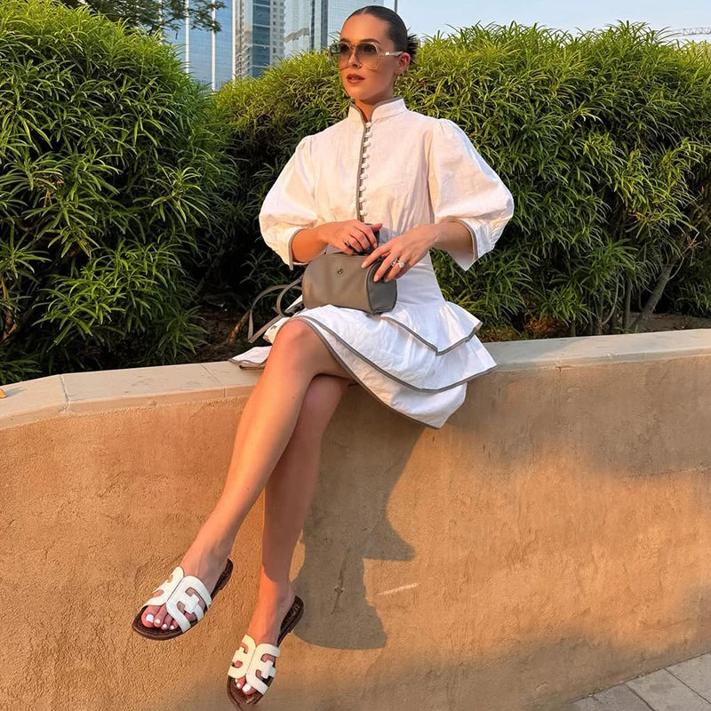 Woman in a contrast patchwork office lady mini dress in white with puff sleeves sitting on a ledge with greenery in the background