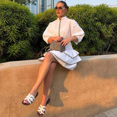 Woman in a  contrast patchwork office lady mini dress in white with puff sleeves sitting on a ledge with greenery in the background
