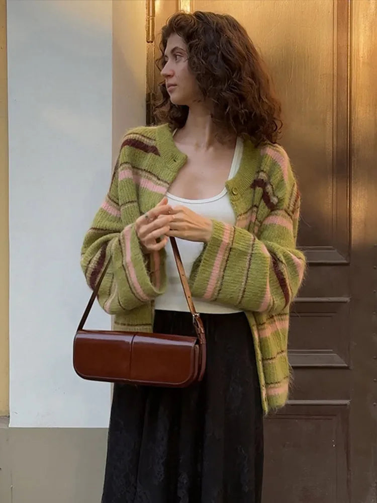 Woman wearing a green and pink striped cardigan holding a brown handbag.