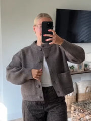 Person wearing a gray cardigan in a room with a TV and decor.