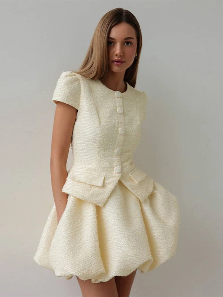 Front angle showing the round neckline, short sleeves, and button detail on a cream textured top paired with a matching mini skirt.