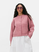 Soft pink crew-neck cardigan styled over a white skirt, showcasing the relaxed fit, button front, and clean minimal silhouette.